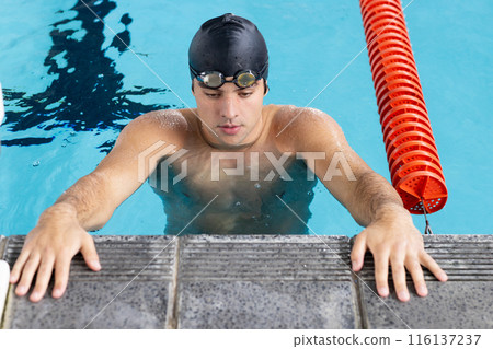 Caucasian young male swimmer resting at swimming pool edge indoors, looking focused Caucasian young male swimmer resting at swimming pool edge indoors, looking focused 116137237