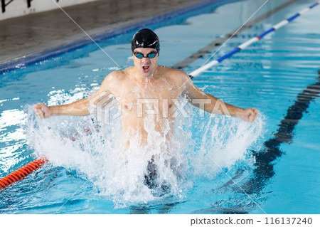 Caucasian young male swimmer training indoors in swimming pool, making a splash Caucasian young male swimmer training indoors in swimming pool, making a splash 116137240
