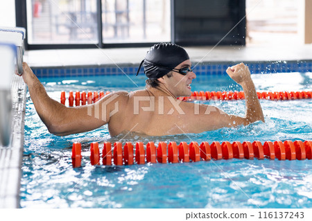 Caucasian young male swimmer with dark hair is training indoors in a pool Caucasian young male swimmer with dark hair is training indoors in a pool 116137243