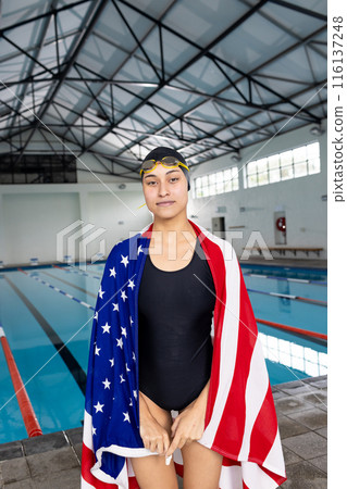 A biracial young female swimmer standing by pool indoors, copy space 116137248