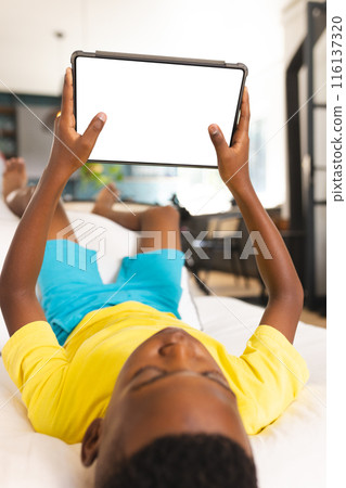 An African American boy holding tablet at home, wearing a yellow shirt, copy space An African American boy holding tablet at home, wearing a yellow shirt, copy space 116137320