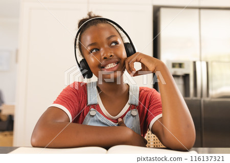 An African American girl wearing headphones, smiling during video call at home 116137321