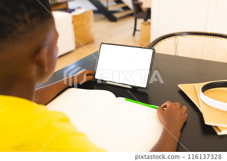 At home, African American boy holding green pen, looking at a tablet, copy space 116137328