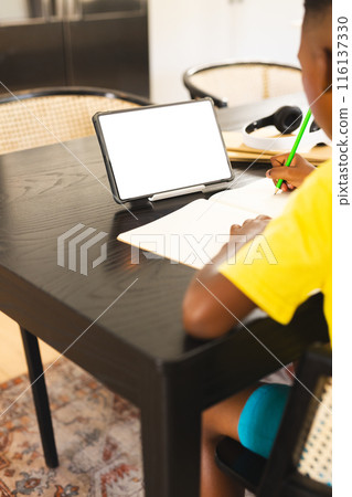African American boy in yellow shirt writing in notebook using tablet, copy space African American boy in yellow shirt writing in notebook using tablet, copy space 116137330