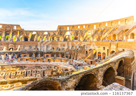 A view of the Colosseum in Rome, Italy, during a beautiful sunset. The ancient amphitheater is bathed in warm light as the sun sets on the horizon. 116137367