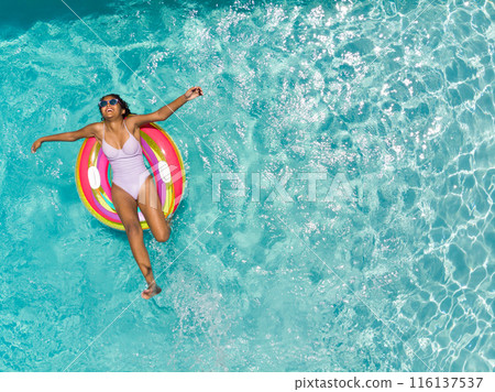 Teenage Biracial girl enjoys a refreshing swim in a pool with copy space on a sunny day 116137537