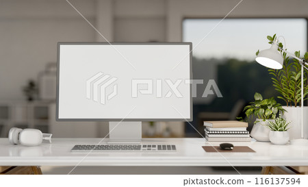 A modern office features a computer with a white-screen mockup and decor on the table. 116137594