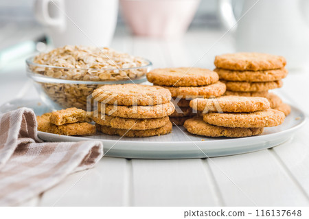 Tasty oatmeal cookies and rolled oat on plate on white table. Tasty oatmeal cookies and rolled oat on plate on white table. 116137648