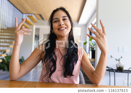 Biracial young woman sitting at home, talking with hands raised on a video call Biracial young woman sitting at home, talking with hands raised on a video call 116137815