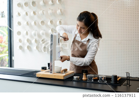 A beautiful young Asian female barista is working in a coffee shop, making a coffee with a machine. 116137911
