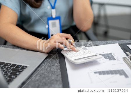 A close-up image of a businesswoman or female accountant using a calculator, working at her desk. 116137934