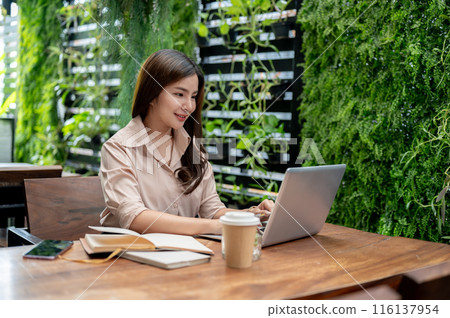 A beautiful Asian woman working remotely from a coffee shop, working on her laptop computer. A beautiful Asian woman working remotely from a coffee shop, working on her laptop computer. 116137954