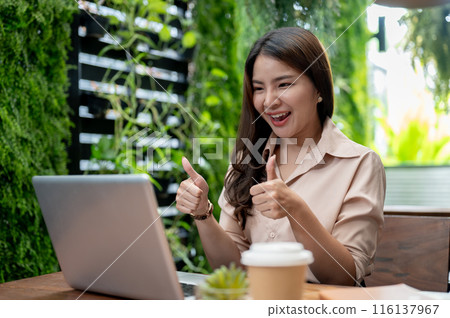 A cheerful Asian businesswoman is showing her thumbs up, having an online meeting, working remotely. 116137967