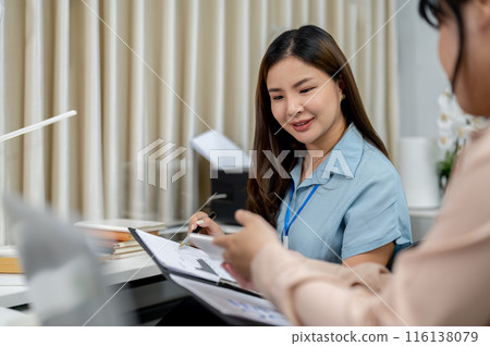 An Asian businesswoman is talking to her colleague, discussing work, working together in the office. 116138079