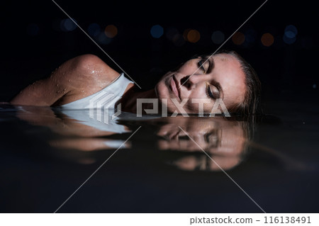 Caucasian woman in a white dress bathes in the night sea. The girl in the water in the evening poses beautifully at sunset on vacation. Relaxation, rest and enjoyment, meditation in the river. Caucasian woman in a white dress bathes in the night sea. The girl in the water in the evening poses beautifully at sunset on vacation. Relaxation, rest and enjoyment, meditation in the river. 116138491