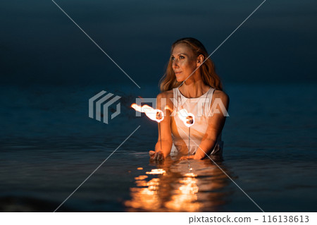 Caucasian woman in a white dress juggles with fireballs in the sea. Fire and water at night. Fire show on the waterfront. High quality FullHD footage. slow motion video 116138613
