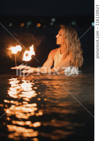 Caucasian woman dancing with fire in the water. Fire show at sea. Acrobatics on the beach. Yoga and relaxation at sunset. Spectacular circus performance. model body. High quality FullHD footage.  116138623