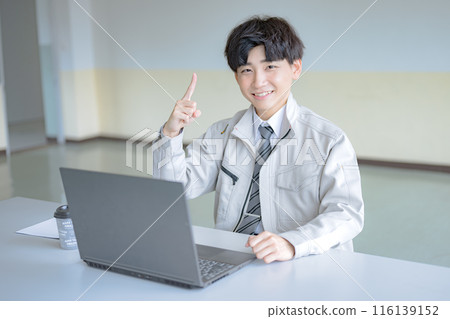 A young man in work clothes pointing at a PC A young man in work clothes pointing at a PC 116139152