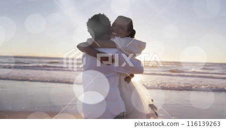 Image of light spots over happy african american bride and groom embracing on beach at wedding Image of light spots over happy african american bride and groom embracing on beach at wedding 116139263