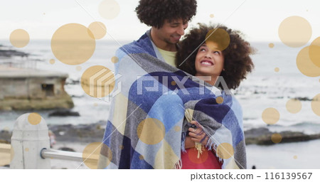 Image of light spots over biracial couple covered in blanket embracing on beach Image of light spots over biracial couple covered in blanket embracing on beach 116139567
