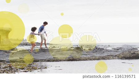 Image of light spots over biracial couple holding hands and walking on beach Image of light spots over biracial couple holding hands and walking on beach 116139571