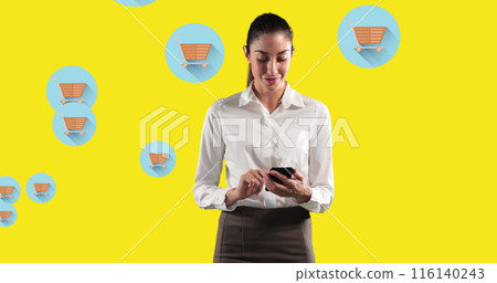 Image of woman using smartphone against multiple shopping cart icons on yellow background 116140243
