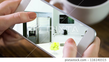 Image of person using smartphone with house kitchen interiors displayed on screen 116140315