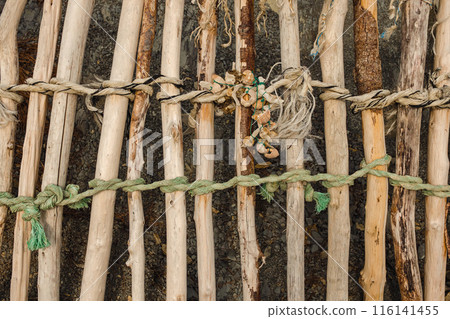A close-up of a wooden structure made from sticks tied together with various ropes and twine, creating a rustic and handmade appearance. A close-up of a wooden structure made from sticks tied together with various ropes and twine, creating a rustic and handmade appearance. 116141455