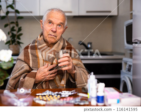 Elderly Senor holding handful of different pills at Home 116141595