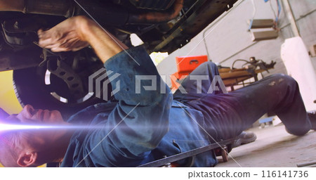 A mechanic wearing blue overalls is fixing car from underneath 116141736