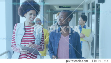 Diverse team walking and talking in office hallway, holding tablets and papers 116141984