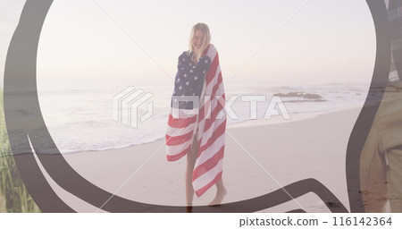 Caucasian female wrapped in American flag stands on beach, smiling Caucasian female wrapped in American flag stands on beach, smiling 116142364
