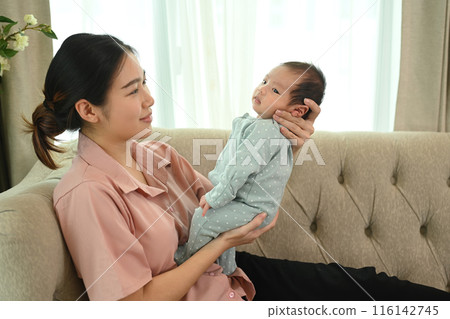 Shot of young Asian mother gently cradling her infant sitting on couch. Child care and motherhood concept 116142745