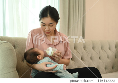 Loving feeding her newborn baby with bottle n the sofa. Healthy infant nutrition and Child Care concept 116142828