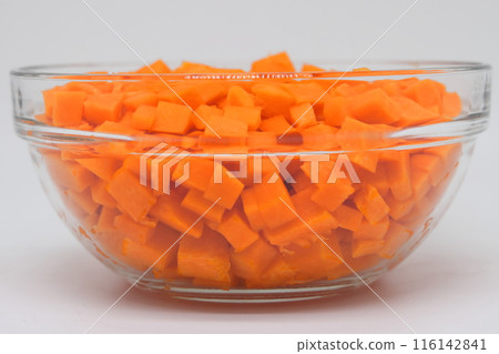 A transparent bowl with diced pumpkin on a white background is ready for cooking. Side view. 116142841