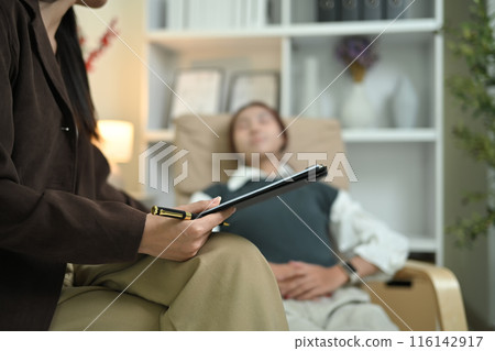 Close up female psychologist taking detailed notes while talking with patient during therapy session 116142917