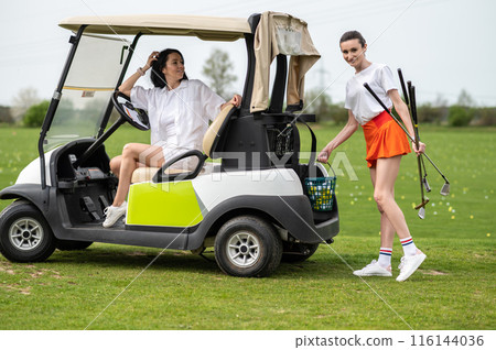 Attractive golfer women posing on course at golf car 116144036