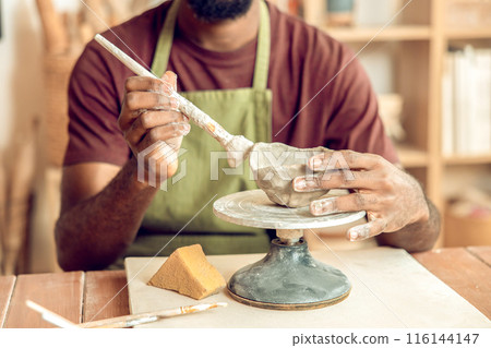 Male sculptor working on a new clay mug in his office Male sculptor working on a new clay mug in his office 116144147