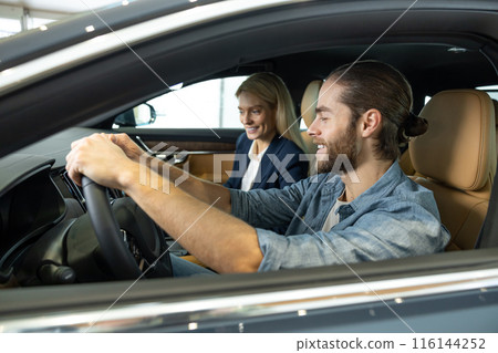 Young bearded man looking excited while sitting in a car before the test drive 116144252