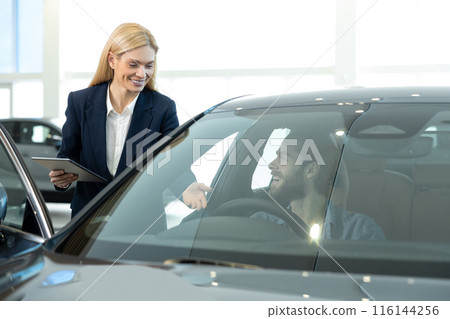 A young man sitting in a new care before the test drive 116144256