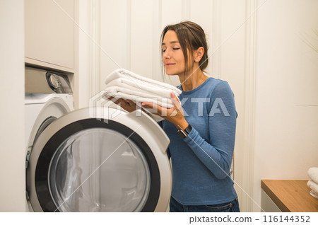 Woman smelling newly washed towels and looking contented 116144352