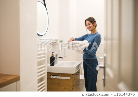 Dark-haired woman holding a pile of white towels in hands Dark-haired woman holding a pile of white towels in hands 116144370