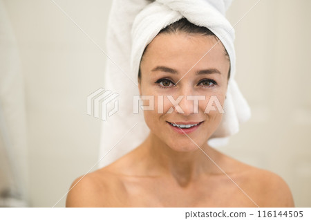 Cute caucasian woman with towel on her head looking contented Cute caucasian woman with towel on her head looking contented 116144505