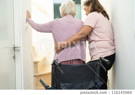 Caregiver help asian or elderly old woman sitting wheelchair support up the stairs in home. Caregiver help asian or elderly old woman sitting wheelchair support up the stairs in home. 116145069