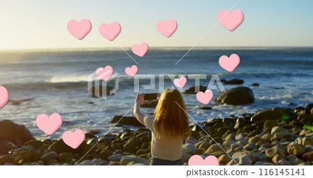 Image of hearts over back view of caucasian woman taking photo on beach Image of hearts over back view of caucasian woman taking photo on beach 116145141