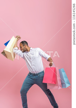 Funny strong African American man wearing shirt and glasses with shopping bags in hands kissing his biceps Funny strong African American man wearing shirt and glasses with shopping bags in hands kissing his biceps 116145266