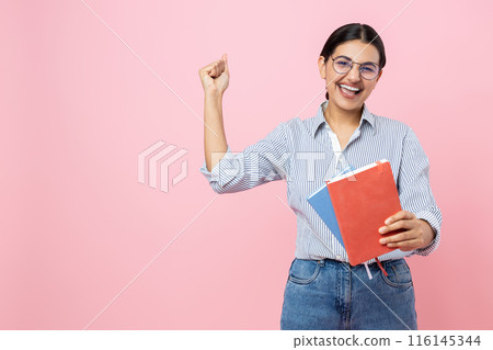 Extremely happy girl in casual shirt holding books rejoicing success clenched fist copy space Extremely happy girl in casual shirt holding books rejoicing success clenched fist copy space 116145344