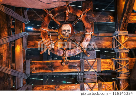 wooden steering wheel with skull in interior of captain's cabin on ancient medieval pirate ship 116145384