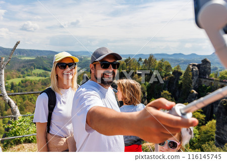 Happy family people travel hiking enjoy shooting selfie at Saxon Switzerland Bastei National park scenic landscape background on sunny summer say. Man make photo video holding gimbal gadget 116145745