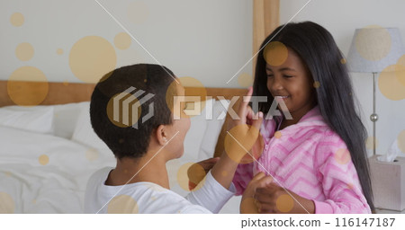 Image of light moving over happy african american mother and daughter putting on pyjama 116147187